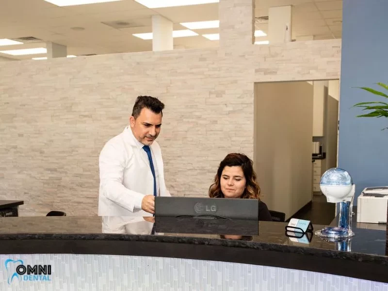 Dr. Bilus Poles at the front desk with a team member at Omni Dental in Arlington Heights