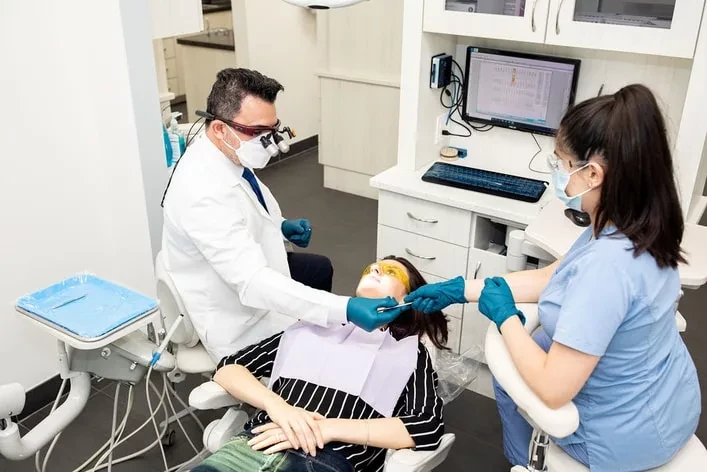 Dr. Bilus Poles wearing magnification loupes while treating a patient with a dental assistant